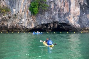Canoe paddling toward a limestone sea cave across emerald water at Hong Island, Phang Nga Bay