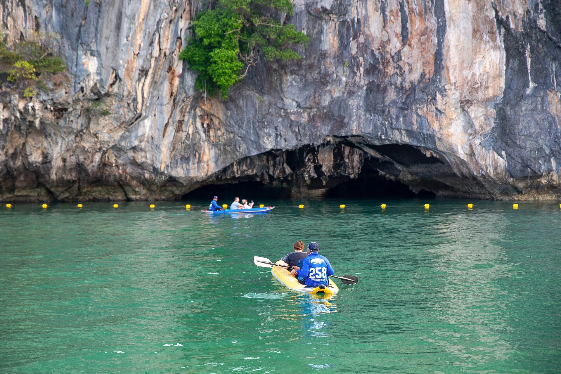 Canoe paddling toward a limestone sea cave across emerald water at Hong Island, Phang Nga Bay