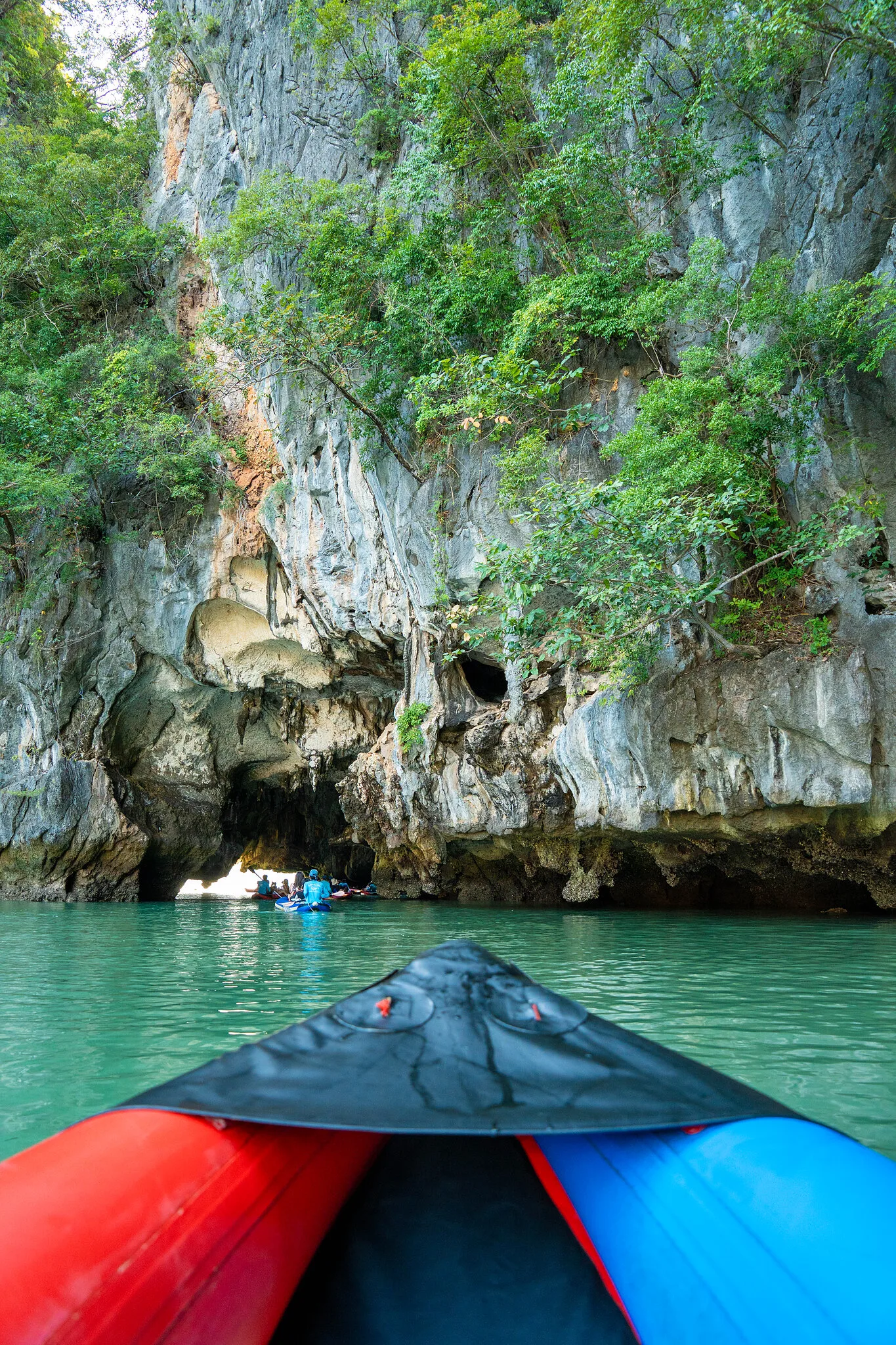View from a canoe bow approaching a limestone cliff and cave opening in Phang Nga Bay