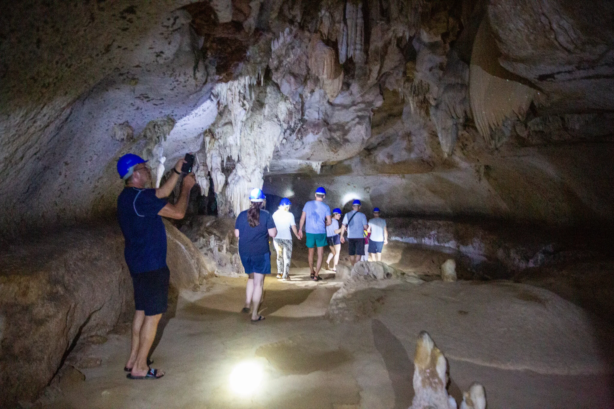 Guide with headlamp leading a small group through a limestone cave with stalactites, Phang Nga Bay