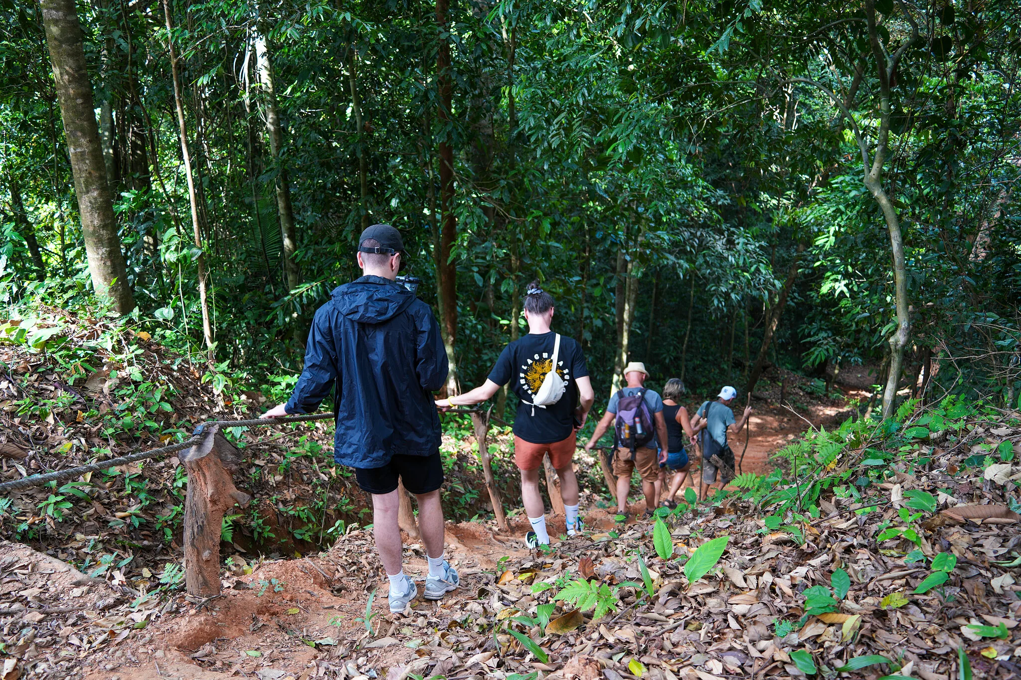 Small group trekking down a leafy rainforest trail toward the waterfall near Khao Lak