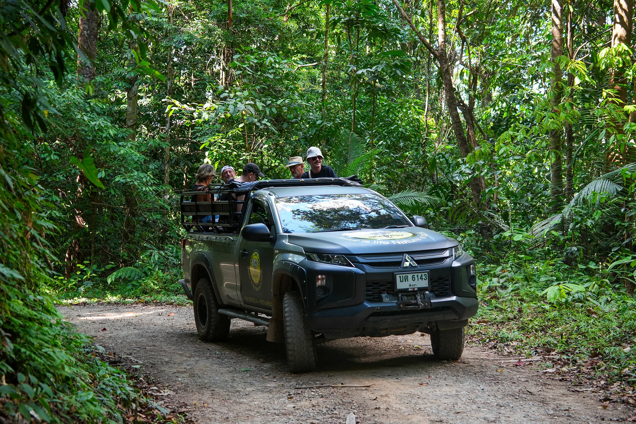 Safari 4x4 with guests standing in the back driving a dirt track through dense jungle