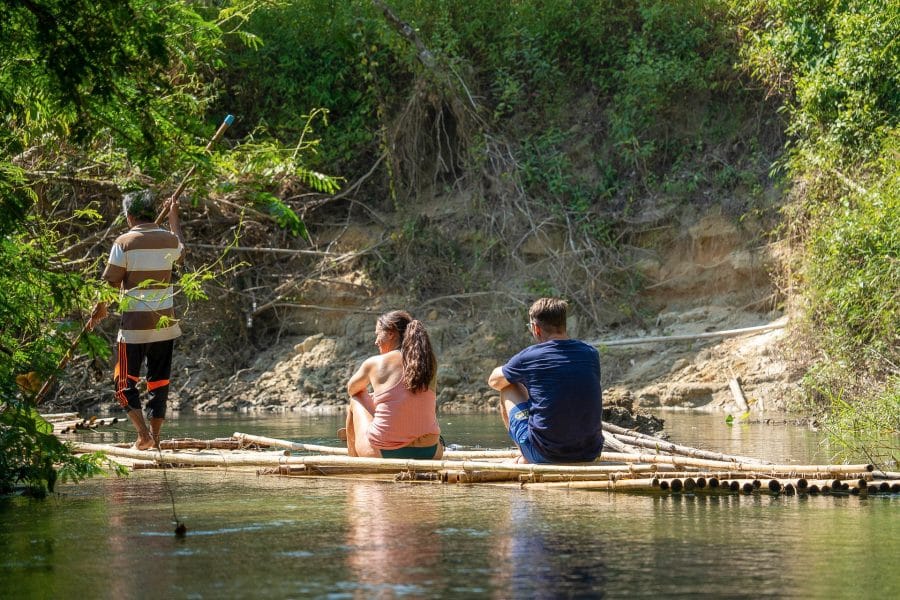 Guide poling a bamboo raft with two guests down a calm jungle river near Khao Lak