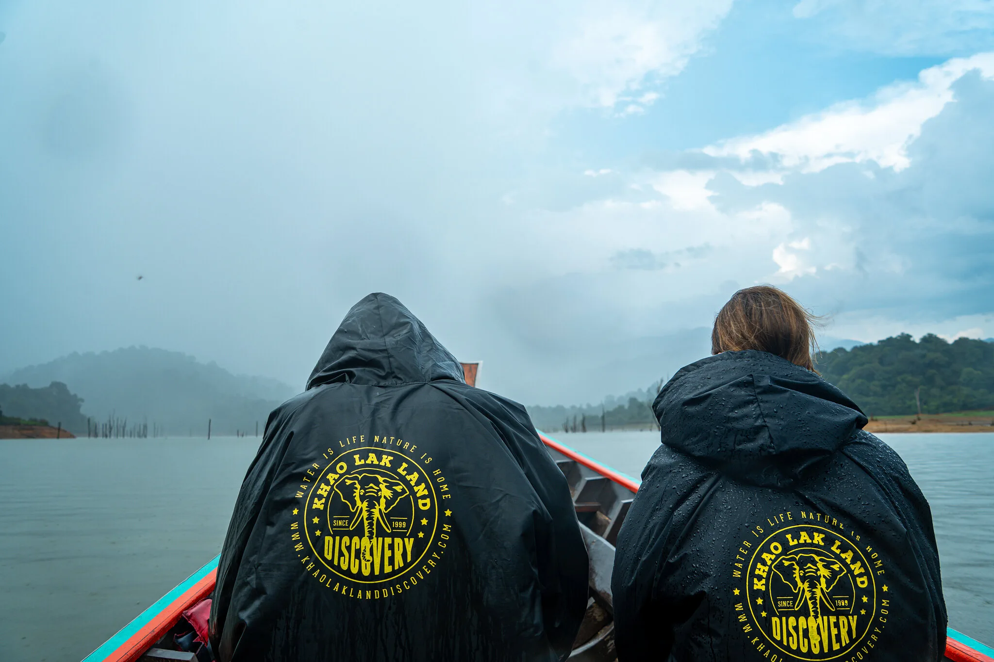 Reisende in KLLD-Regenjacken auf einem Longtail-Boot über den nebligen Cheow-Lan-See, Khao Sok
