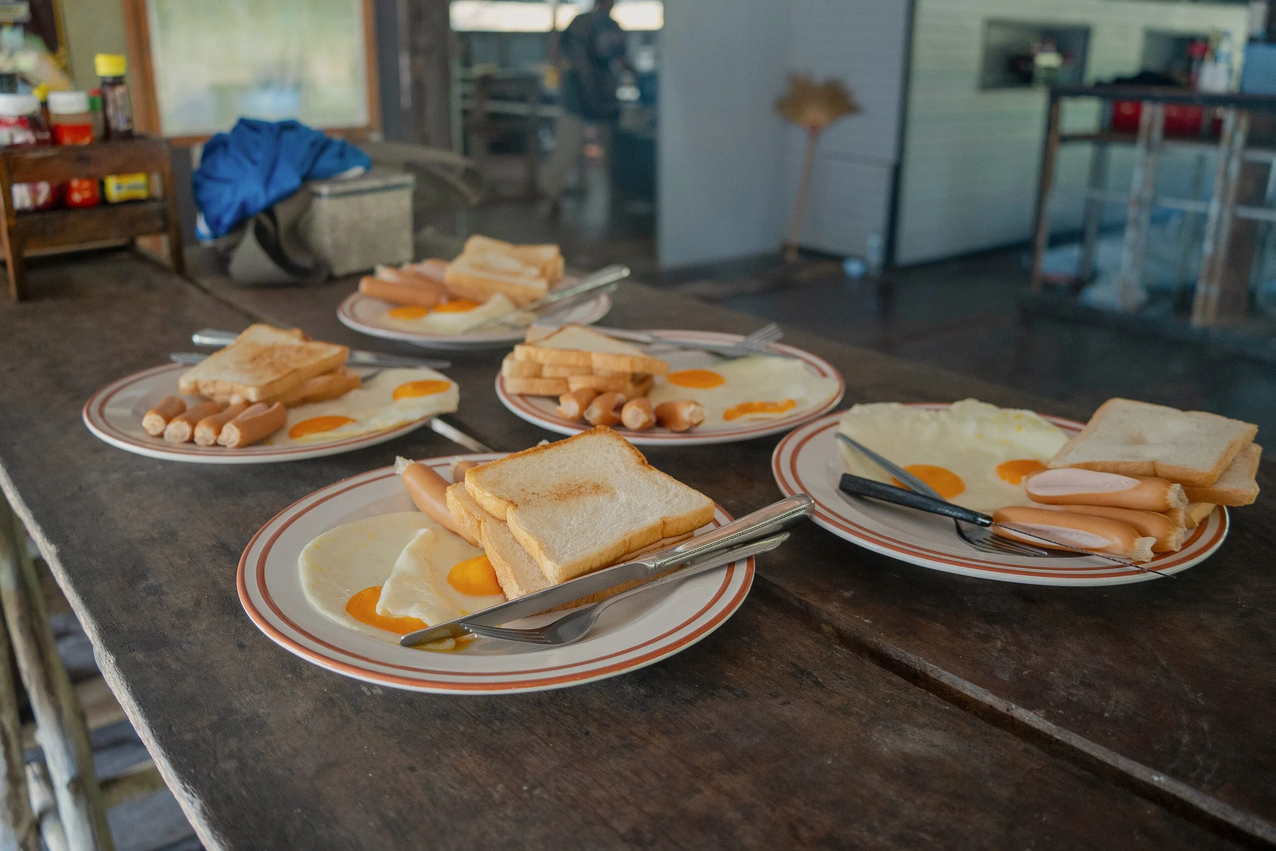 Frühstück mit Spiegeleiern, Toast und Würstchen auf dem Tisch im schwimmenden Floßhaus auf dem Cheow-Lan-See