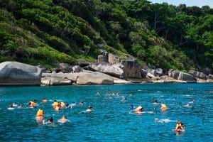 Snorkelers in orange life vests swimming near granite boulders in the clear sea of the Similan Islands