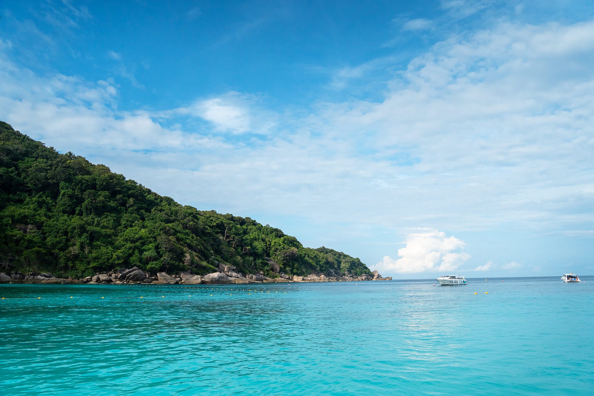 Speedboats anchored off a forested granite island in calm turquoise water, Similan Islands, Thailand