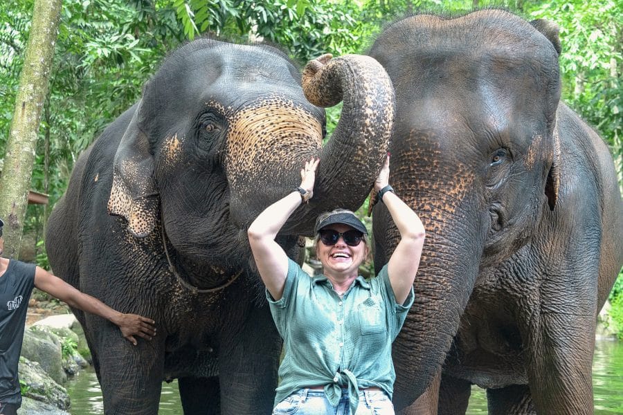 Elephant Bath Khao Lak — a guest laughing with two elephants in a jungle river on an ethical elephant-care tour
