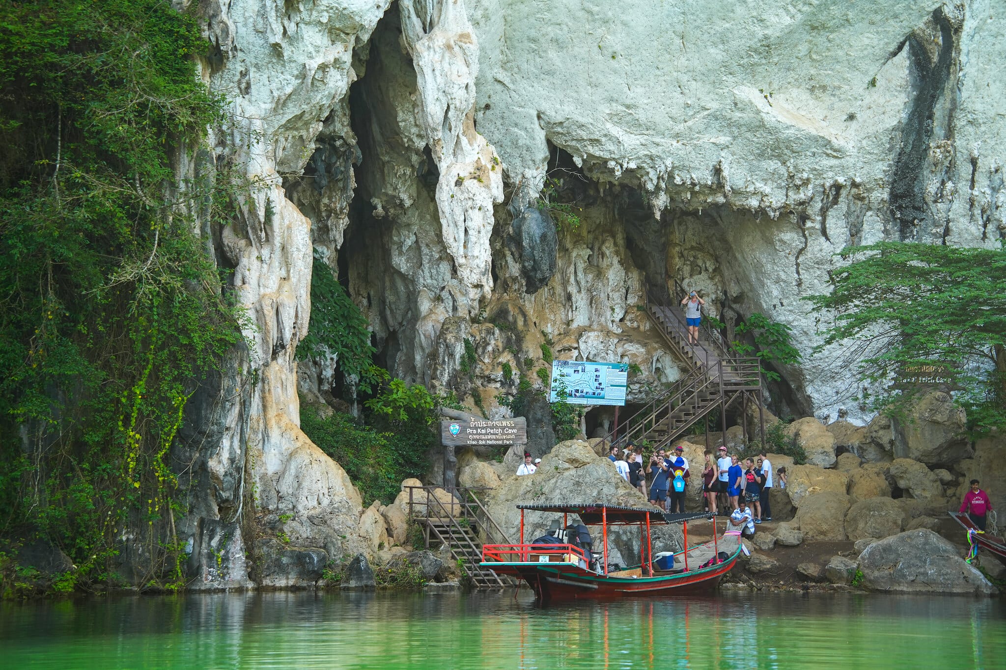Longtail boat moored below a limestone cliff and cave entrance on Cheow Lan Lake, Khao Sok
