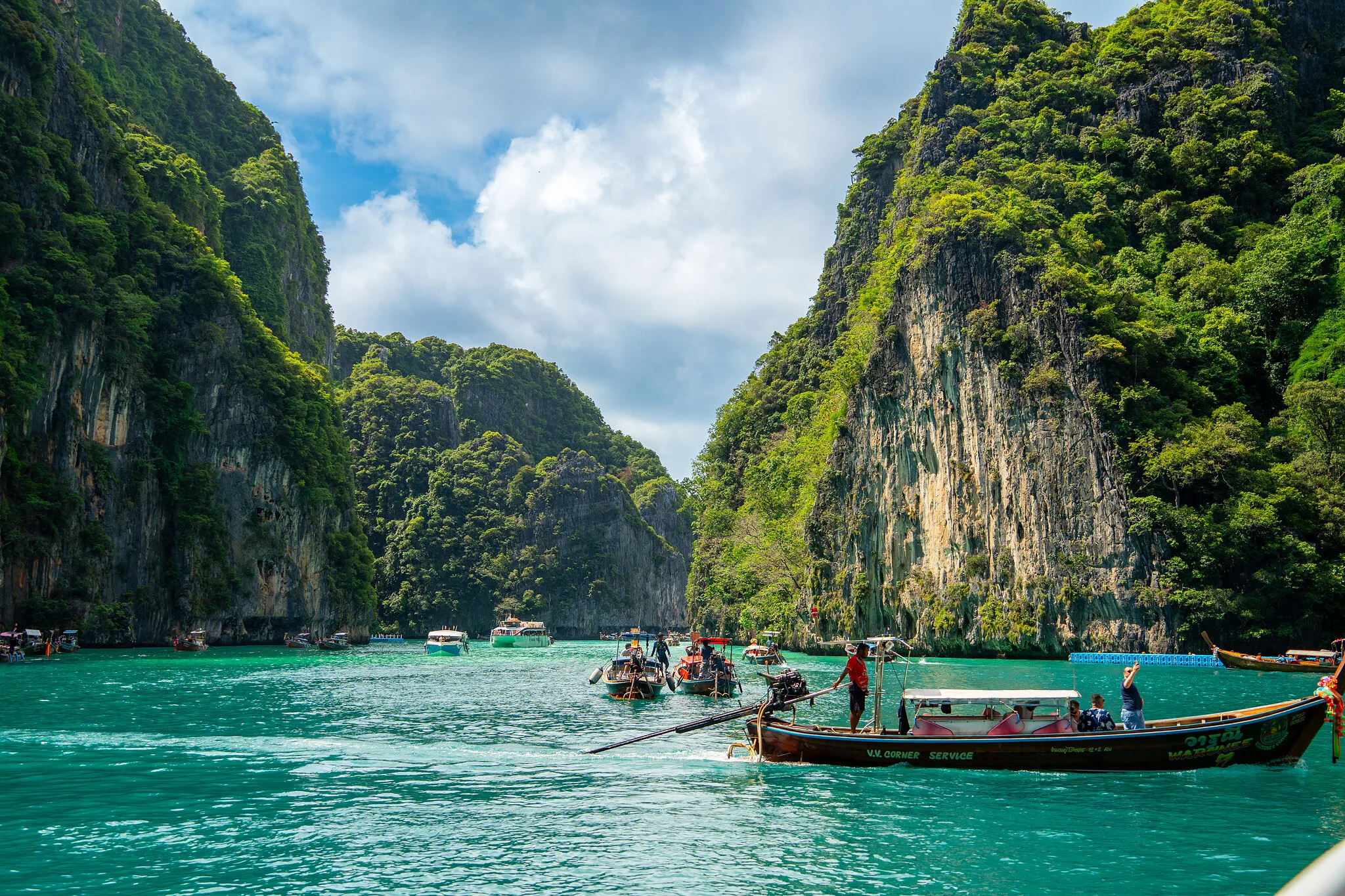 Longtail boats in emerald water between the towering limestone cliffs of Phi Phi Leh
