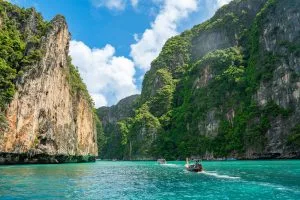 Speedboat crossing turquoise water beneath sheer limestone cliffs at Phi Phi Leh
