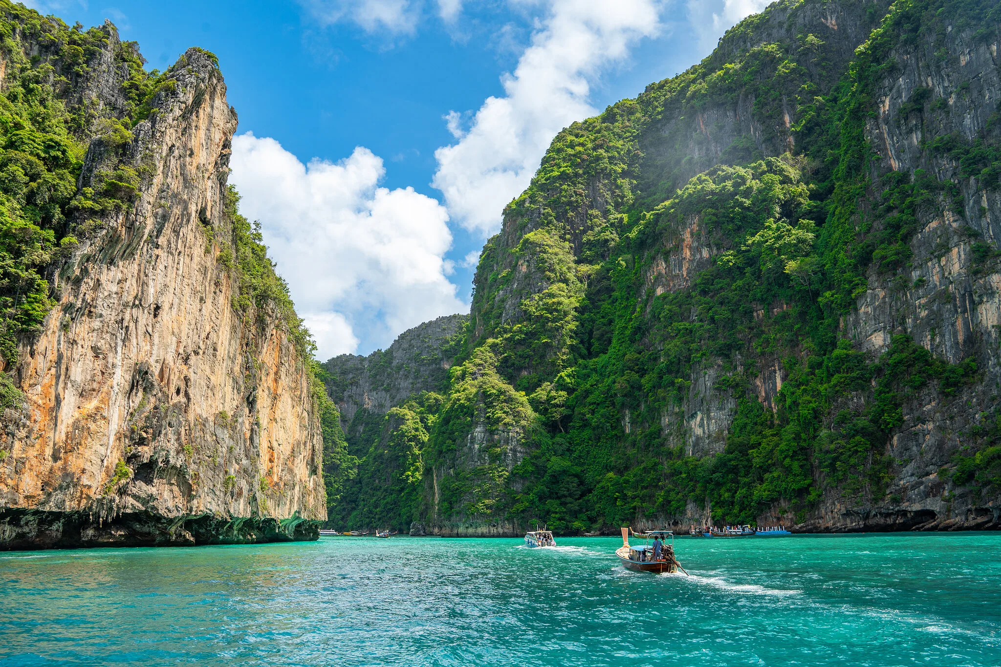 Speedboat crossing turquoise water beneath sheer limestone cliffs at Phi Phi Leh
