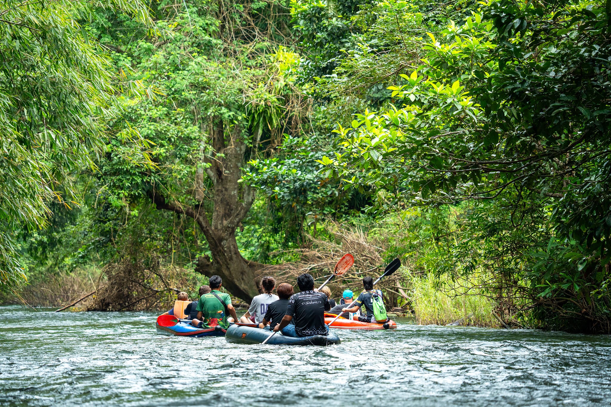 Guests paddling inflatable canoes down the Sok River beneath jungle trees in Khao Sok