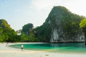 Curved white-sand beach and green water beneath a limestone karst on Koh Hong, Krabi
