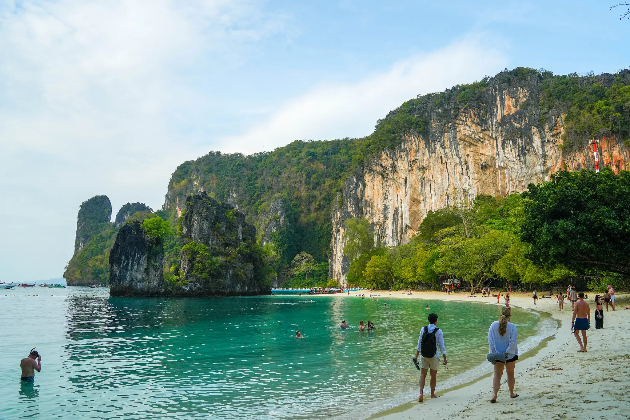 Visitors wading along the shallow turquoise shore beneath towering cliffs on Koh Hong, Krabi