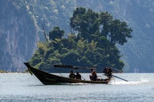 Longtail boat speeding past a jungle-covered karst islet on Cheow Lan Lake, Khao Sok