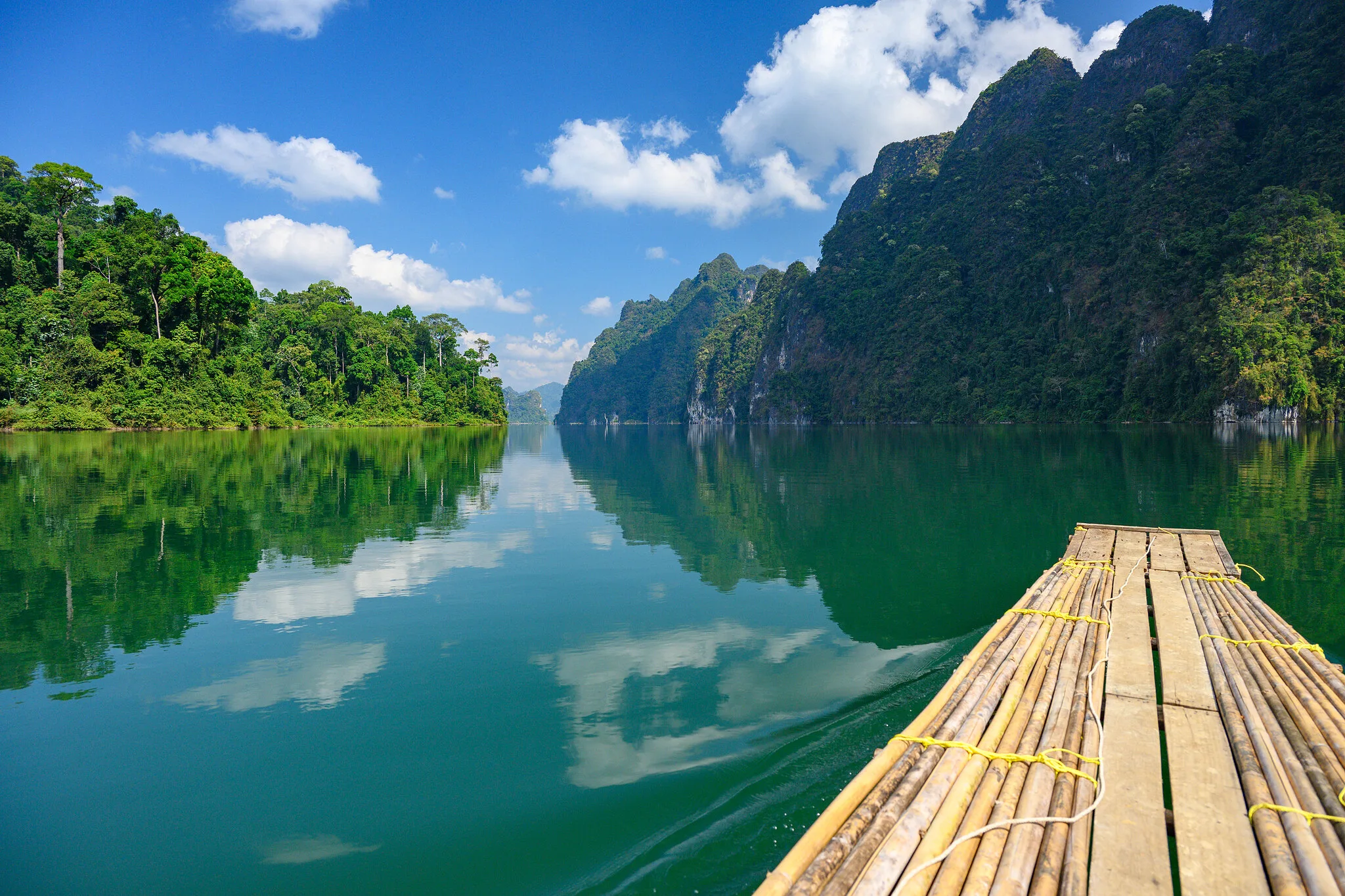 Bamboo raft gliding across emerald Cheow Lan Lake toward limestone peaks, Khao Sok