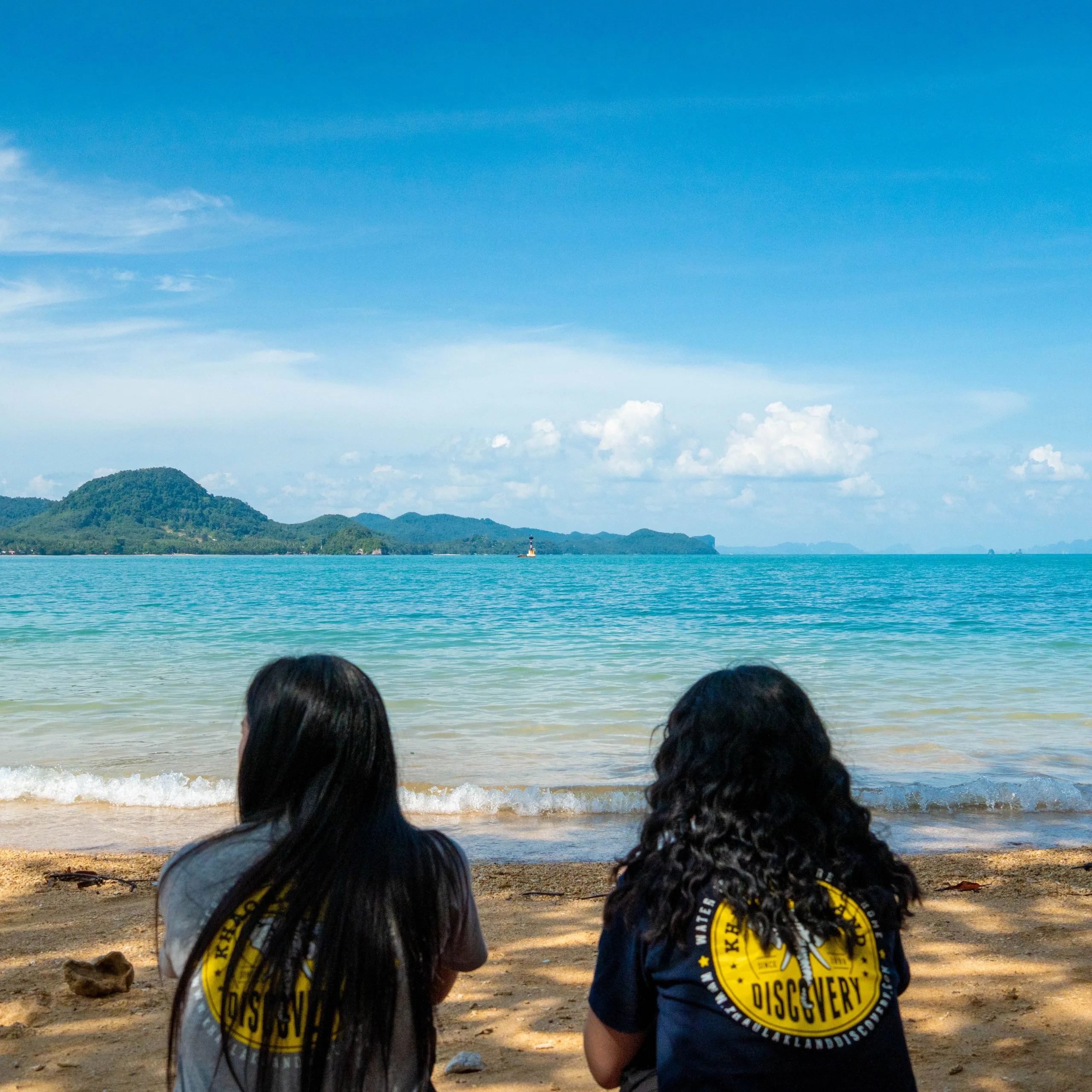 Deux visiteurs en T-shirts Discovery contemplent la mer depuis la plage