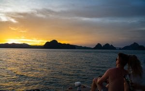 Gäste beobachten vom Katamaran aus den Sonnenuntergang hinter den Kalksteininseln der Phang-Nga-Bucht