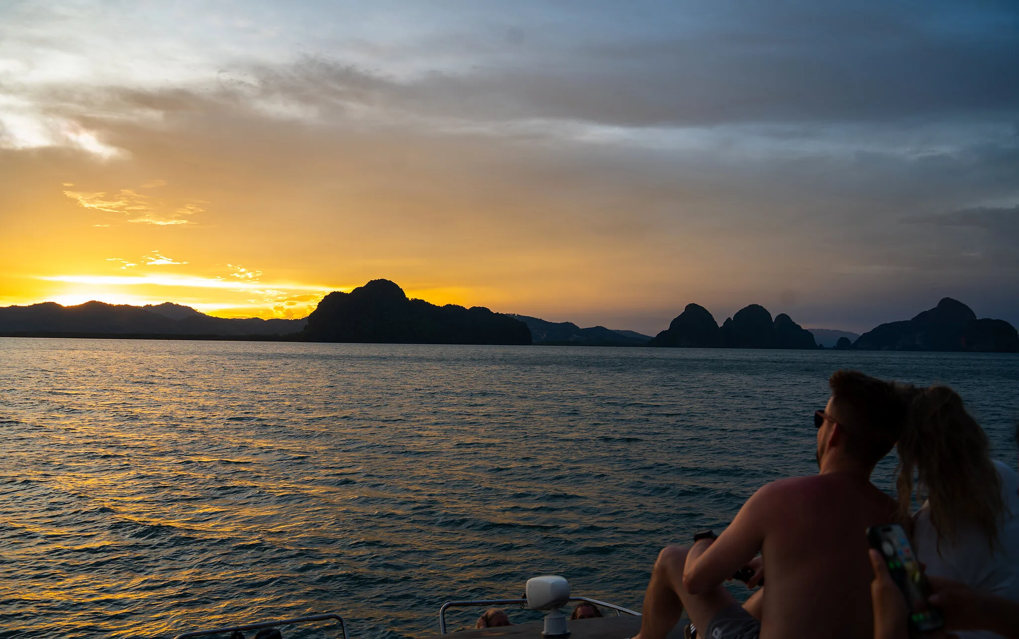 Depuis le catamaran, des visiteurs regardent le soleil se coucher derrière les îles calcaires de la baie de Phang Nga