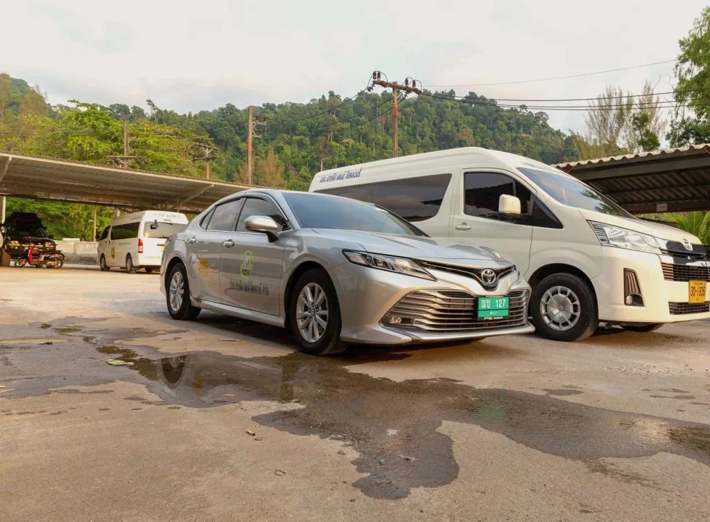 A Toyota Camry and a Toyota Commuter minivan from the Khao Lak Land Discovery fleet, parked with forested hills behind