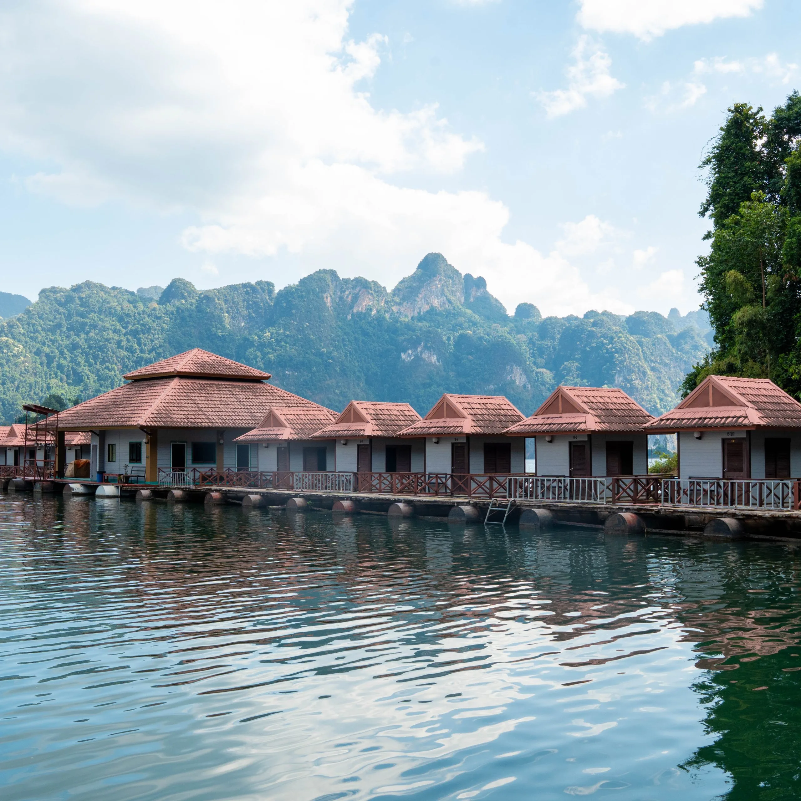 A row of floating bungalows moored on the emerald water of Cheow Lan Lake beneath towering limestone karst peaks in Khao Sok National Park