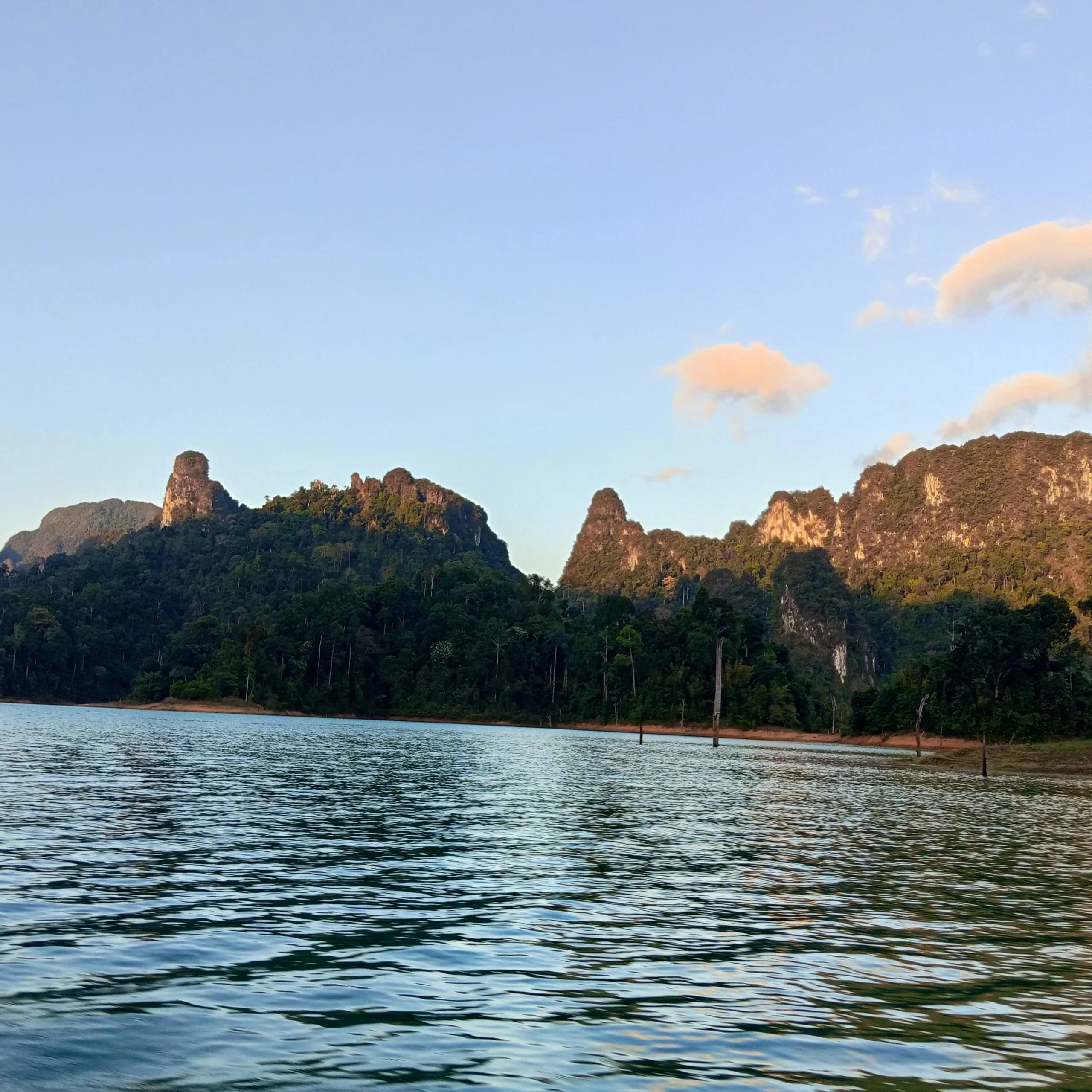 Late afternoon light on jagged limestone peaks rising above the still water of Cheow Lan Lake