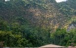 Jungle-covered limestone cliffs rising above the calm emerald water of Cheow Lan Lake beside a floating raft house