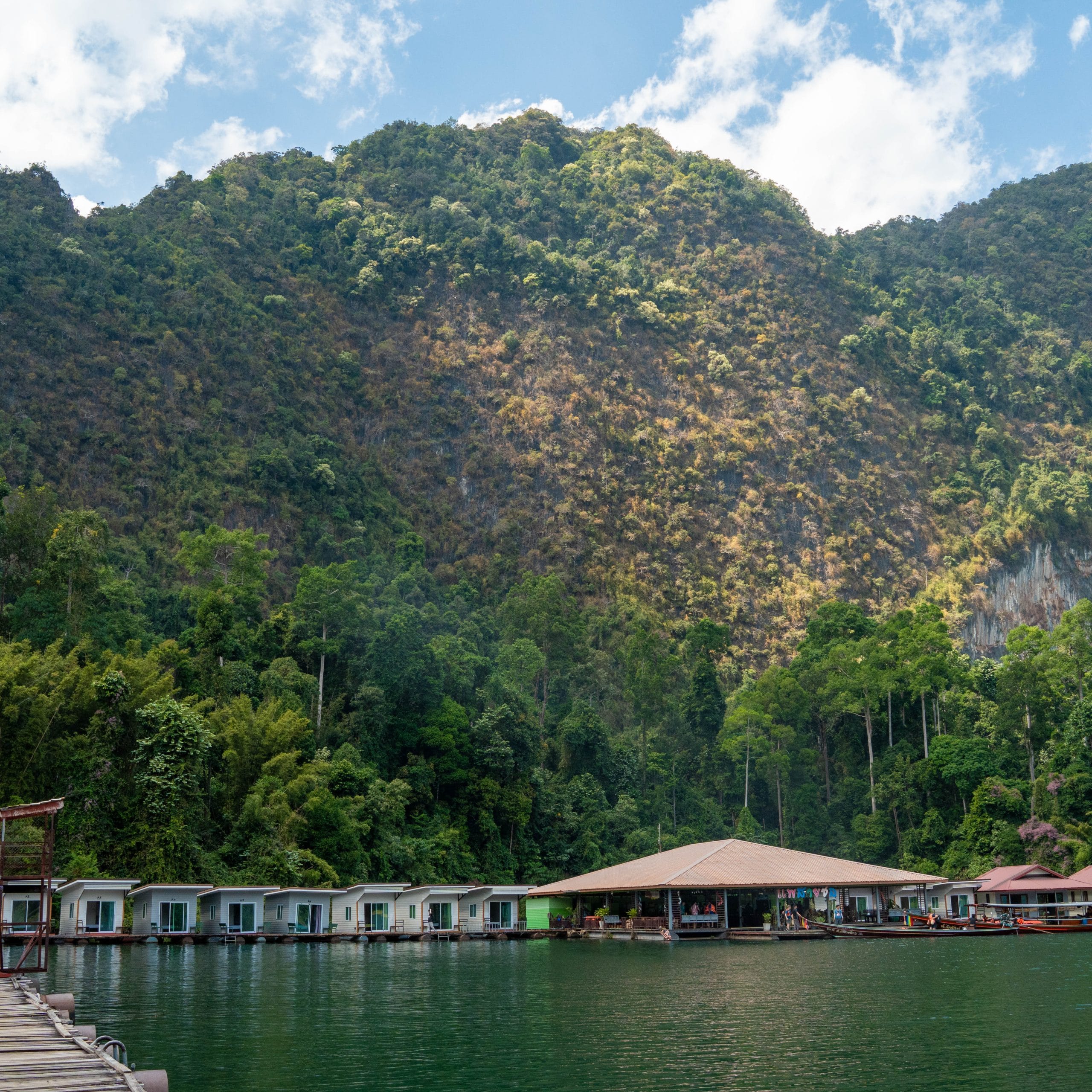 Jungle-covered limestone cliffs rising above the calm emerald water of Cheow Lan Lake beside a floating raft house