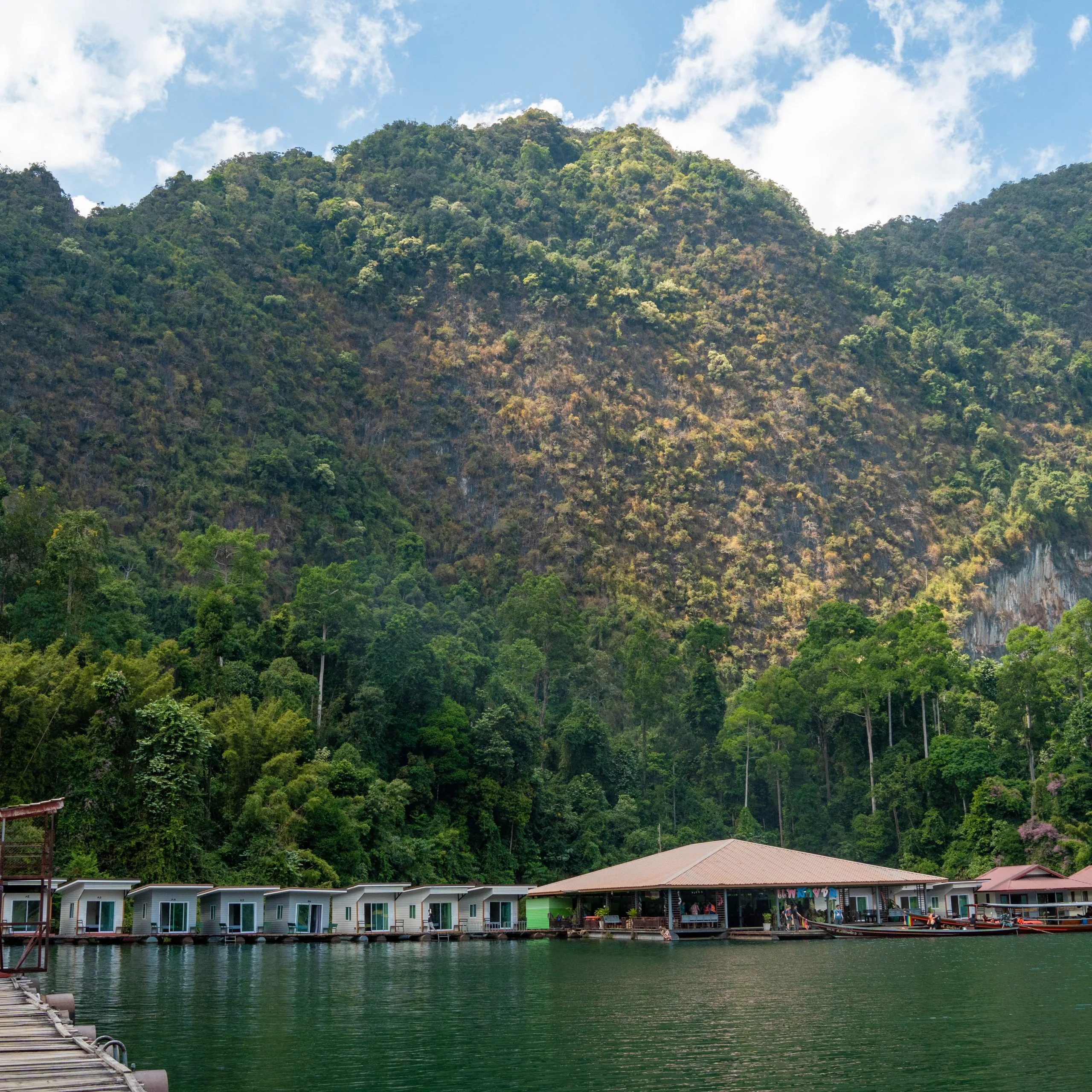 Jungle-covered limestone cliffs rising above the calm emerald water of Cheow Lan Lake beside a floating raft house