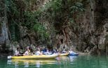 Guests paddle a yellow canoe across an emerald lagoon below jungle-covered limestone cliffs.