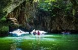 Canoes drift through a vast sea cave opening onto green water at Hong Island in Phang Nga Bay.