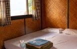 Simple bamboo-walled bedroom inside a floating bungalow on Cheow Lan Lake with towels folded on the bed