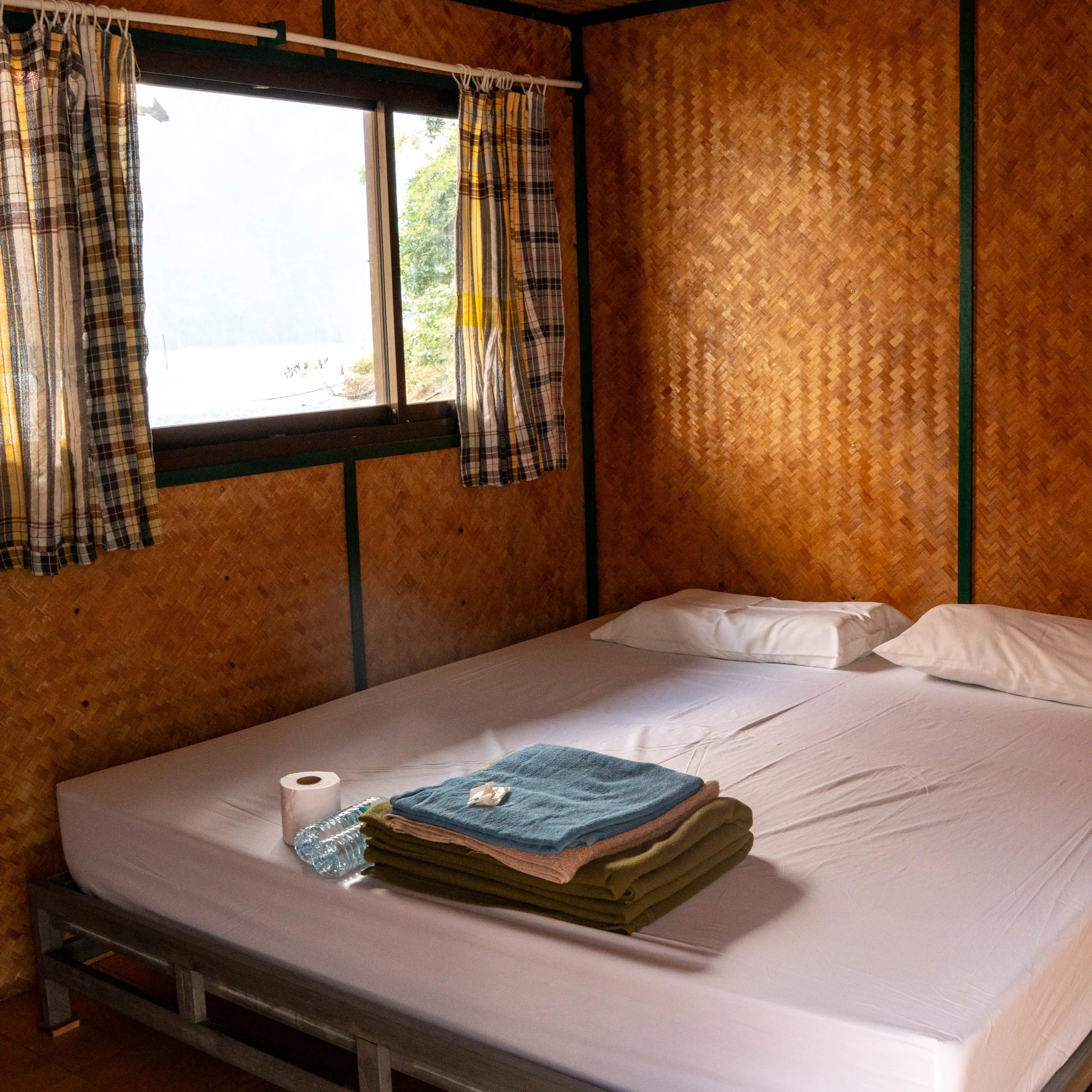 Simple bamboo-walled bedroom inside a floating bungalow on Cheow Lan Lake with towels folded on the bed