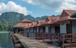A wooden walkway running past red-roofed floating bungalows towards limestone mountains on Cheow Lan Lake