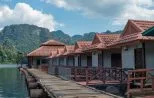 A wooden walkway running past red-roofed floating bungalows towards limestone mountains on Cheow Lan Lake