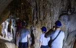 Visitors in safety helmets walk through a limestone cave lined with stalactites in Phang Nga Bay.