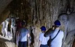 Visitors in safety helmets walk through a limestone cave lined with stalactites in Phang Nga Bay.
