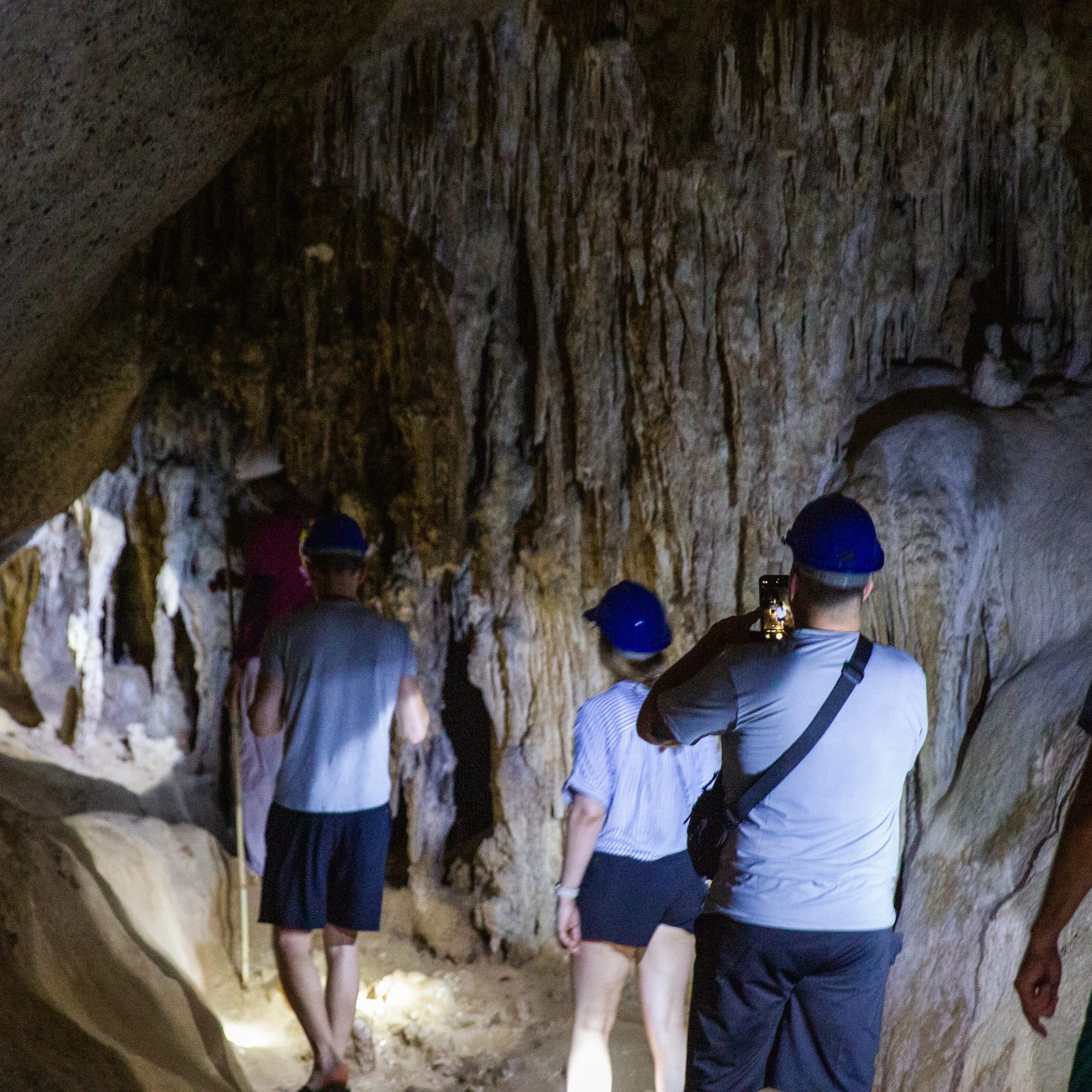 Visitors in safety helmets walk through a limestone cave lined with stalactites in Phang Nga Bay.