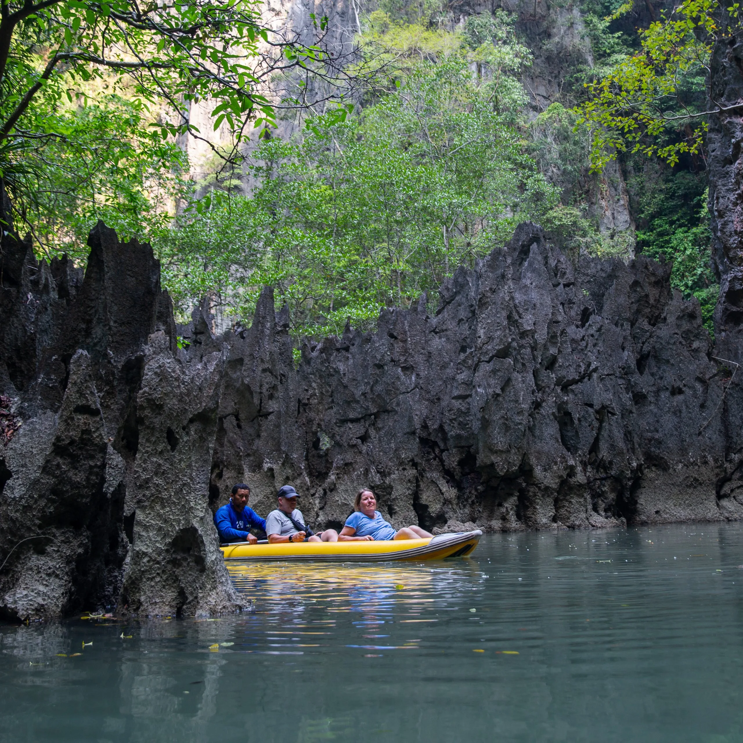 Canoe passengers pass jagged karst rock formations along a sheltered channel in Phang Nga Bay.