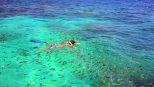 A snorkeller swims above a shoal of small tropical fish in shallow reef water at Phi Phi.