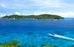 Aerial view of a forested Similan island ringed by coral reef with a speedboat crossing the bay